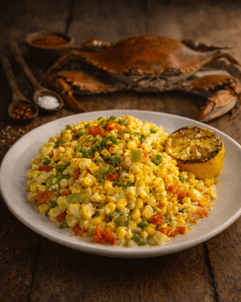 Creamy Corn Maque Choux a Louisiana corn dish served lemon wedge and a steamed crab on a rustic wooden table.