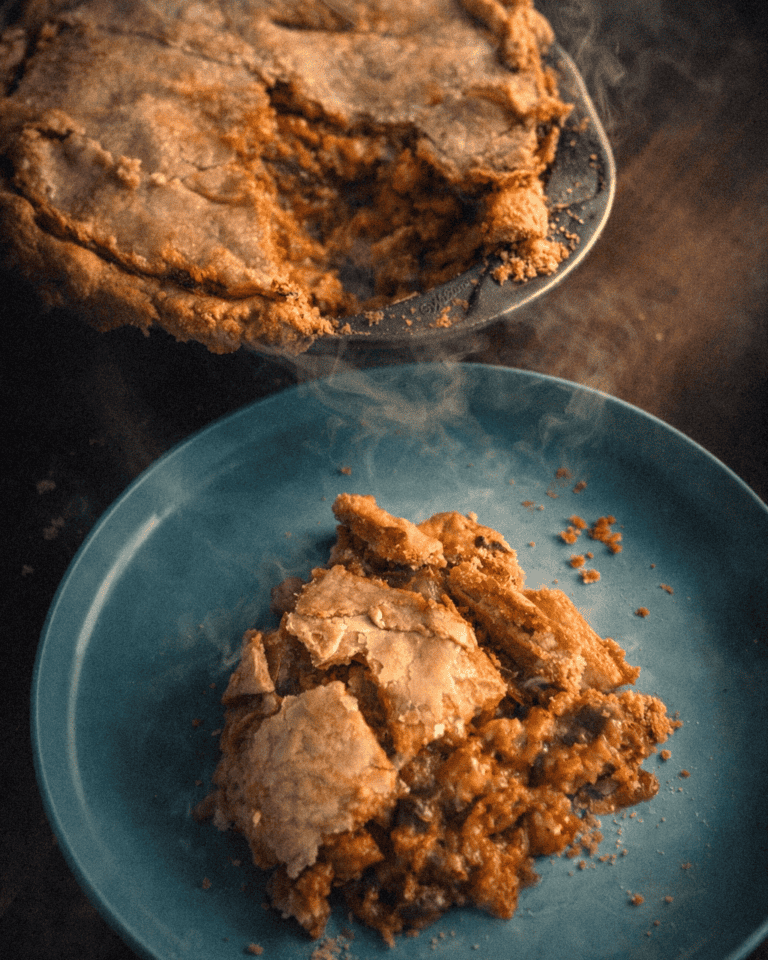 Golden-brown baked Crawfish Pie served on a blue plate with a glass dish with steam coming off the top.