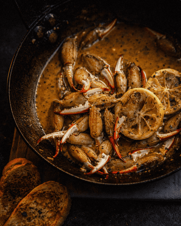 Succulent crab claws cooking in a skillet with lemon slices and flavorful butter and garlic sauce, close-up.