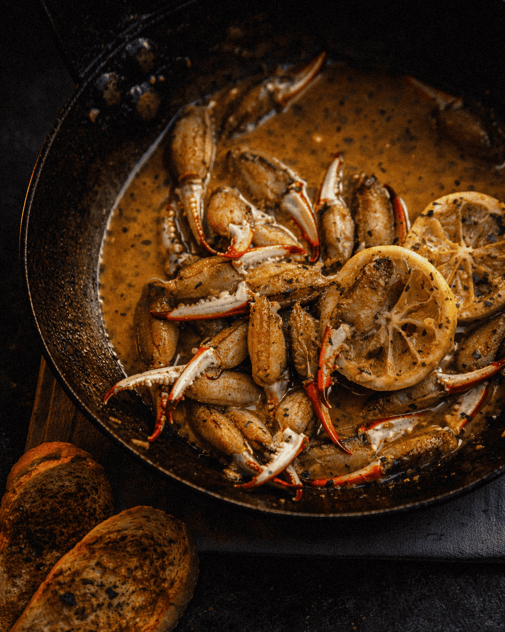 Succulent crab claws cooking in a skillet with lemon slices and flavorful butter and garlic sauce, close-up.