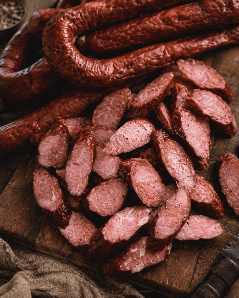 Smoked sausage and sliced meat on a wooden cutting board, perfect for barbecue or charcuterie.