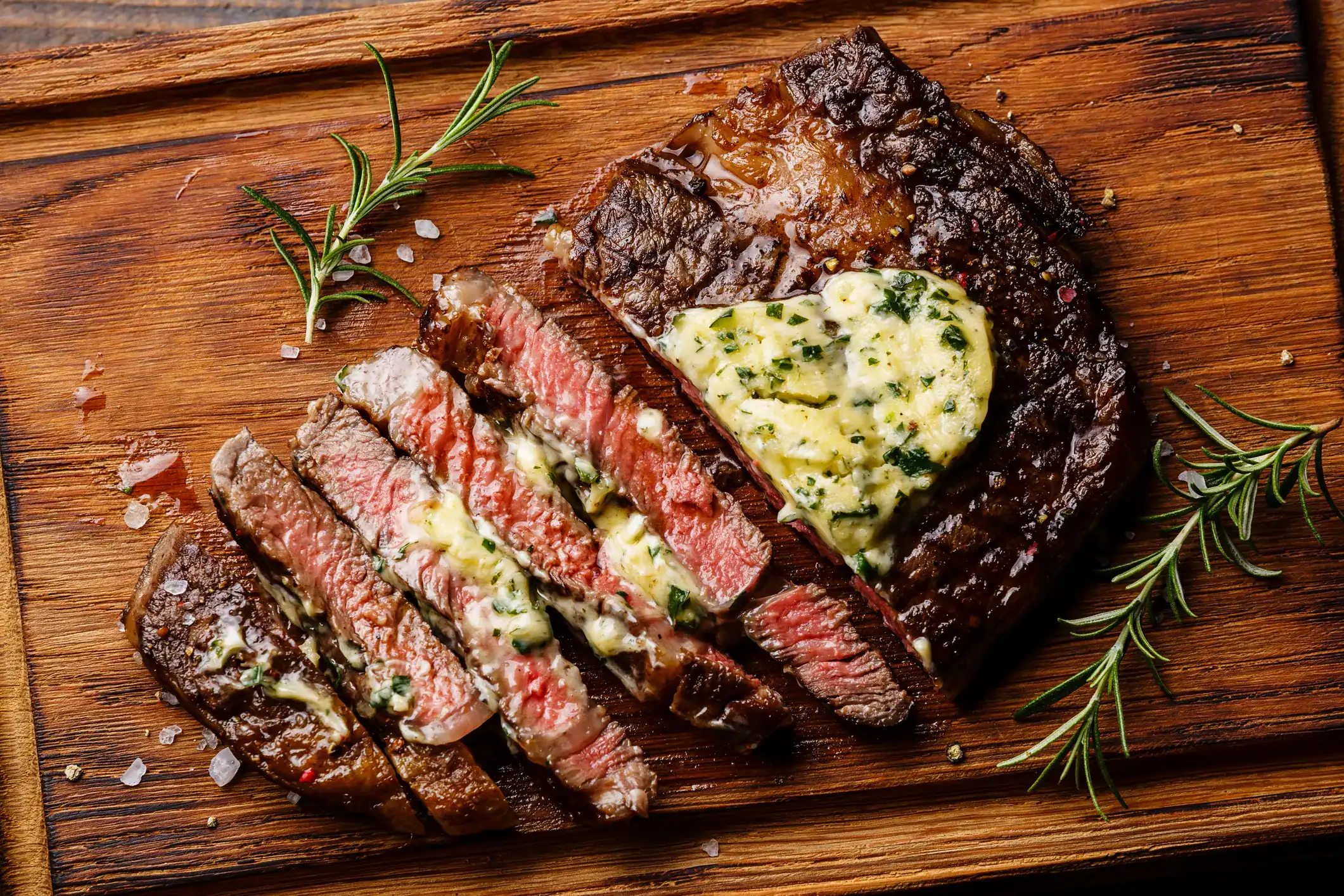 Juicy grilled steak topped with herb butter, sliced and served on a wooden board.
