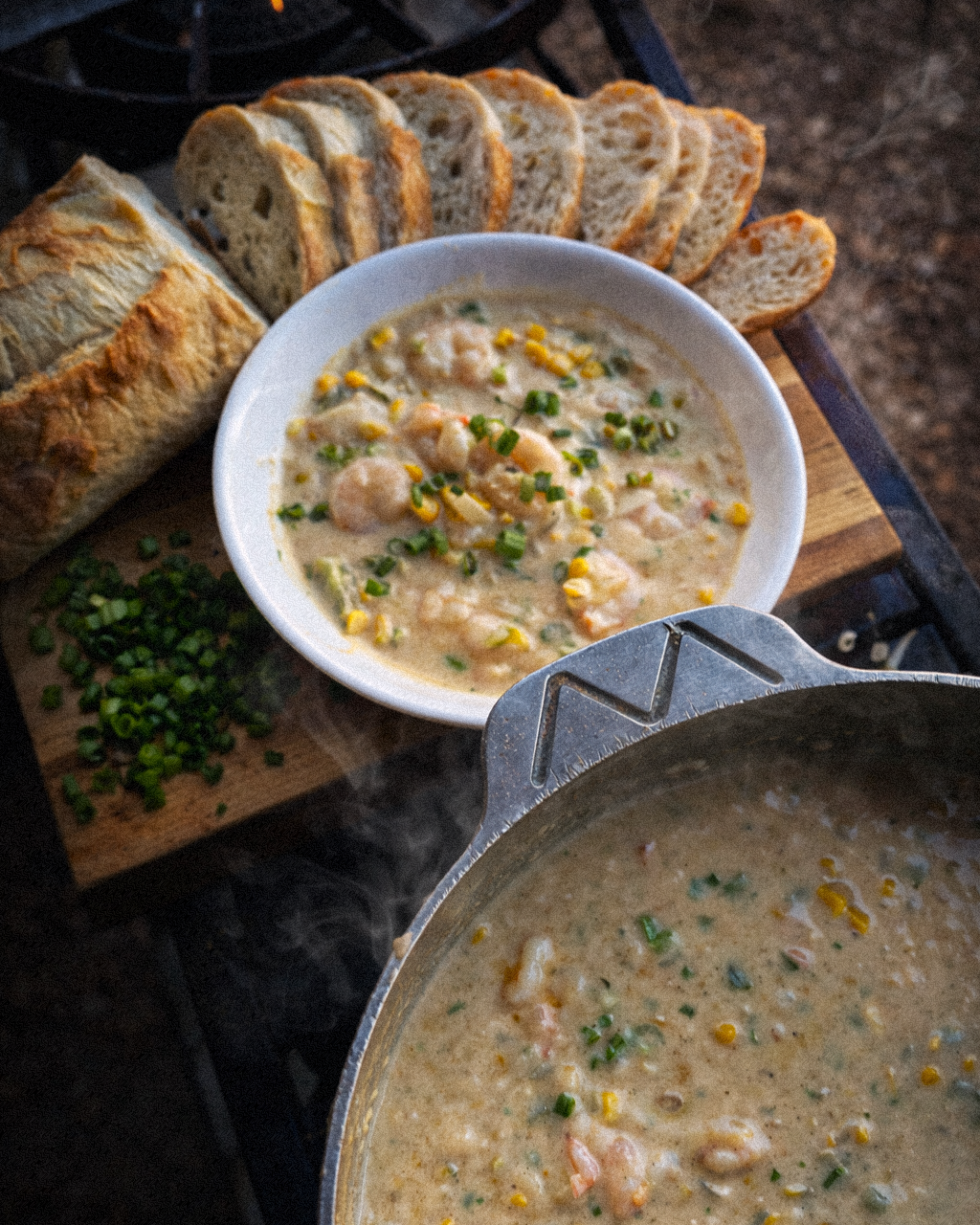 A bowl of shrimp and corn soup garnished with green onions and sliced French bread.