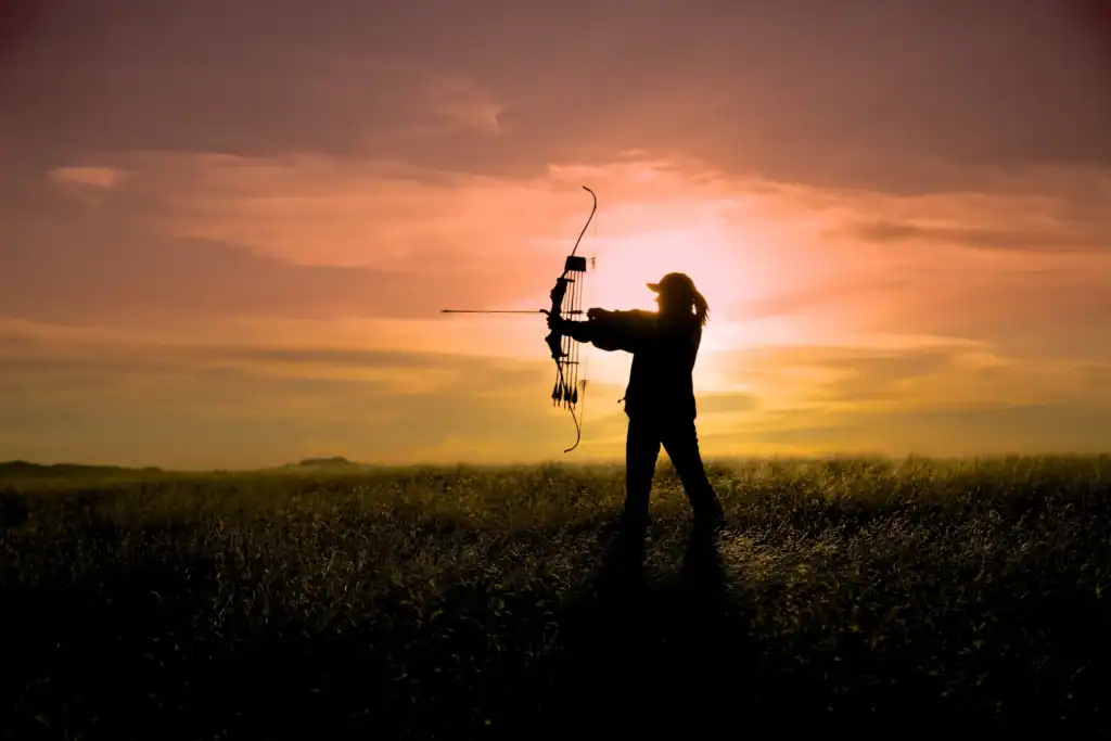 Silhouette of a woman archer aiming a bow in Louisiana at sunset, outdoor scene with vibrant sky.