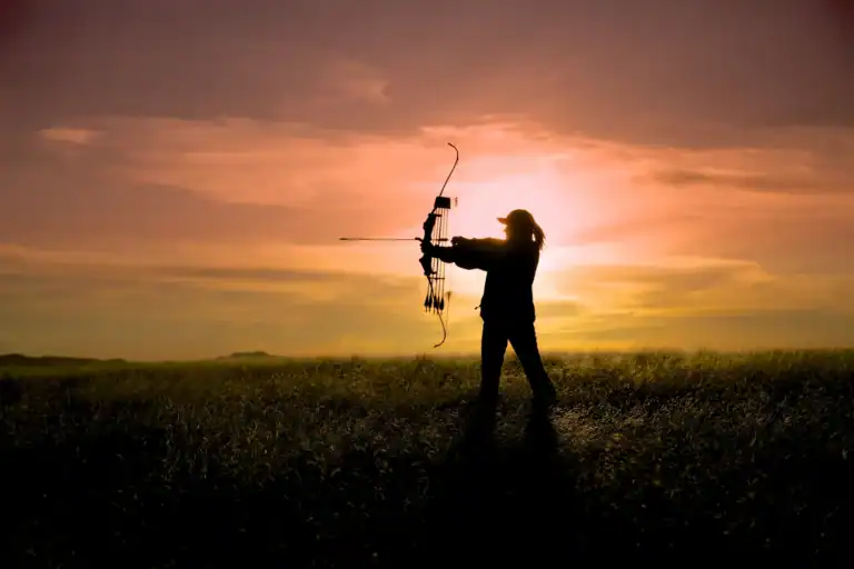 Silhouette of a woman archer aiming a bow in Louisiana at sunset, outdoor scene with vibrant sky.