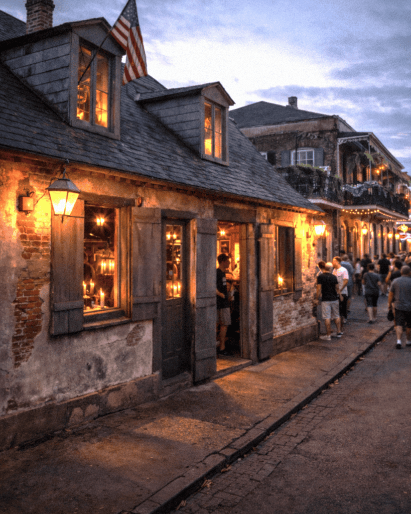 Historic street standing outside Lafittes Blacksmith Bar in New Orleans with cozy restaurants, warm lighting, and pedestrians at dusk.