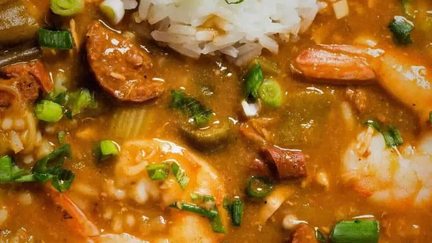 A bowl of Louisiana stew with shrimp and sausage in it served with rice, garnished with green onions.