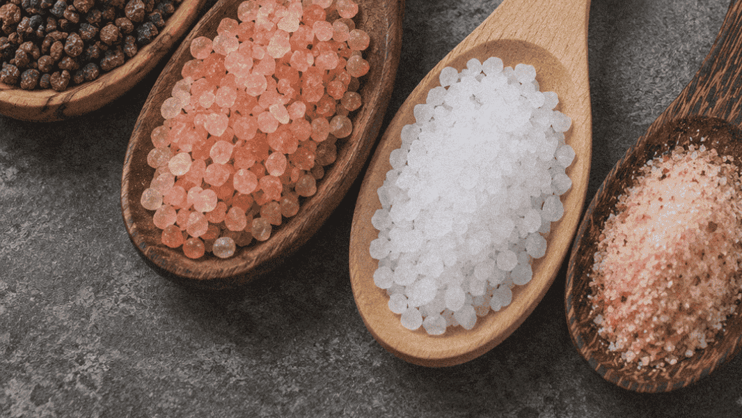 Assorted salts in wooden spoons, including sea salt and Himalayan pink salt.