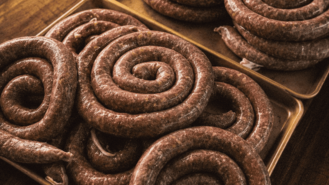 Raw sausage links arranged in a spiral shape on a wooden surface.