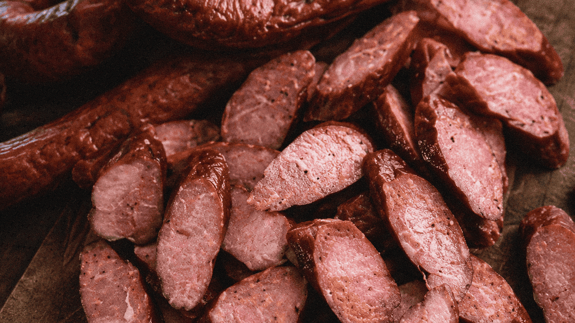 Smoked sausage and sliced meat on a wooden cutting board, perfect for barbecue or charcuterie.