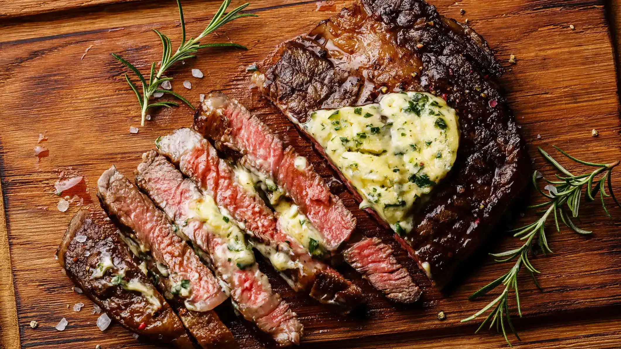 Juicy grilled steak topped with herb butter, sliced and served on a wooden board.