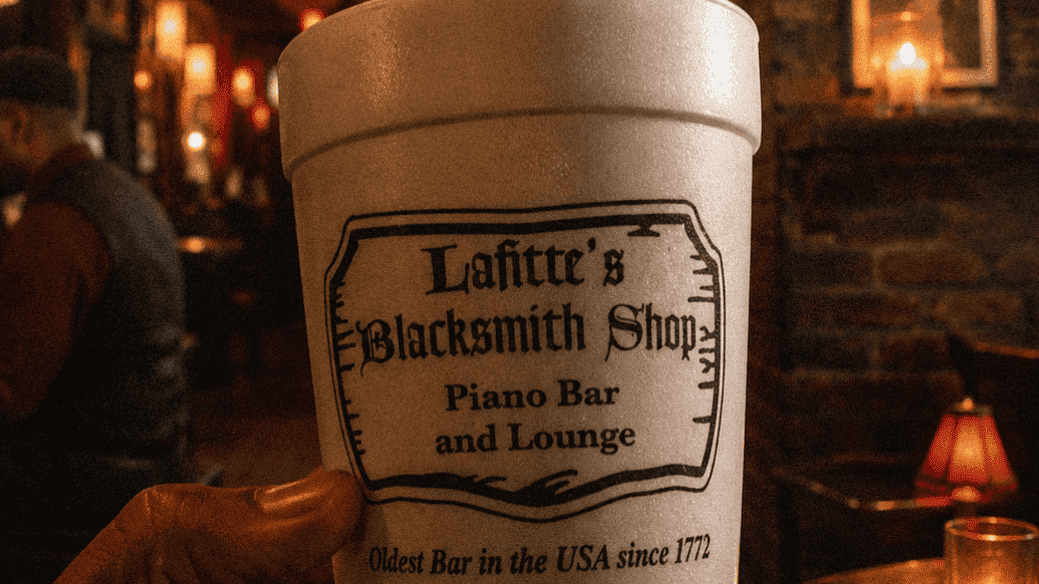 Hand holding a large drink cup at Lafitte's Blacksmith Shop piano bar lounge in New Orleans.