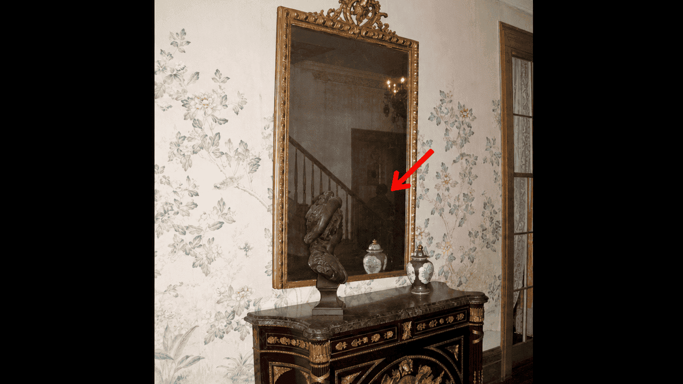 Vintage mirror above ornate Louisiana-style sideboard with floral wallpaper.