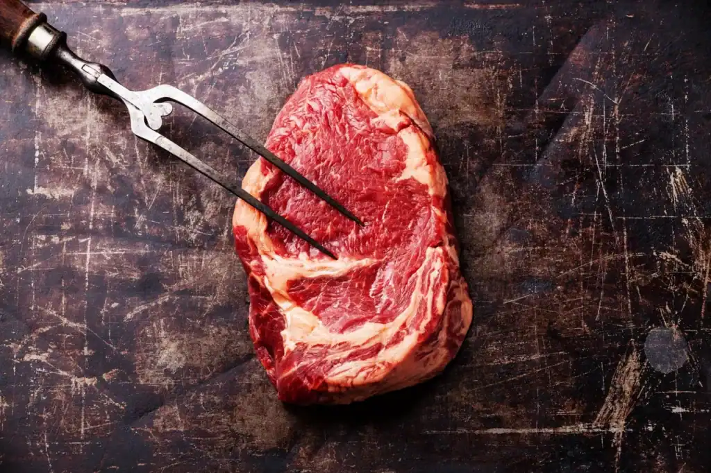 Fresh raw steak on dark wooden surface with meat fork for Cajun cuisine.