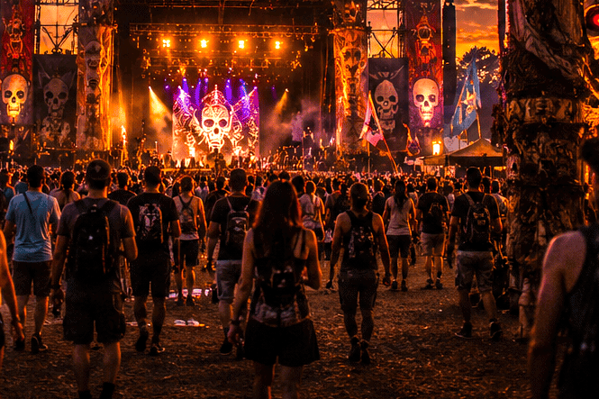 Crowd enjoying a Louisiana music festival at sunset with skull-themed stage decor.