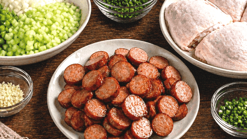Delicious sausage slices, chicken thighs, and fresh chopped vegetables on a rustic wooden table.