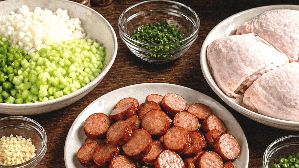 Grilled sausage slices with chopped green onions and raw chicken breasts on a wooden table.
