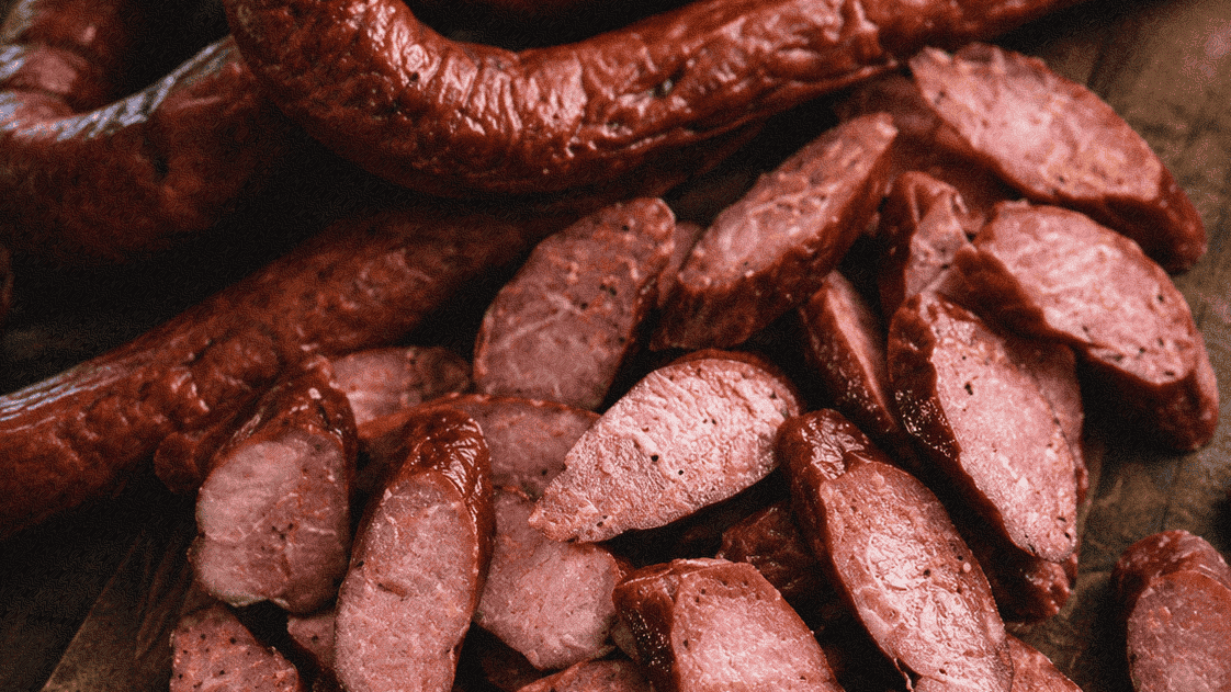 Smoked sausage and sliced meat on a wooden cutting board, perfect for barbecue or charcuterie.